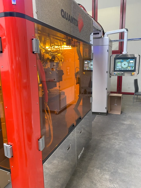 Side view of the Quantix NOVUM digital printing machine showing its interface, orange safety shield and controls.