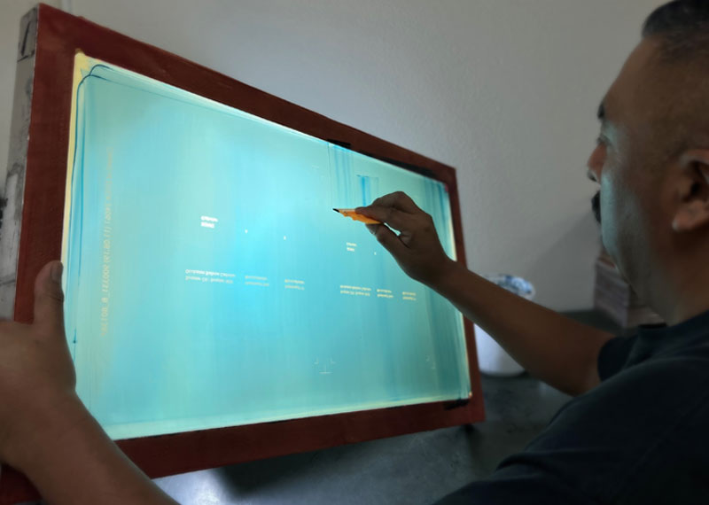 Deco Tech technician inspecting an imaged screen printing screen on a light table
